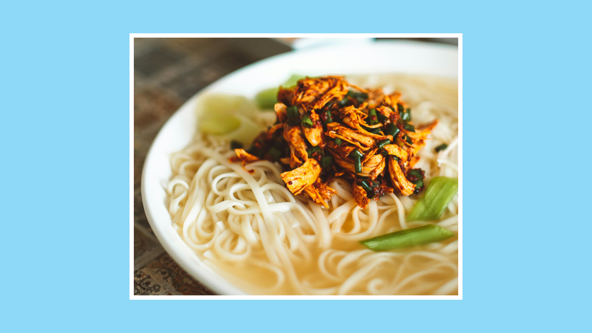 “Bowl of red curry noodle soup with chicken, noodles and spring onions in a light broth.”