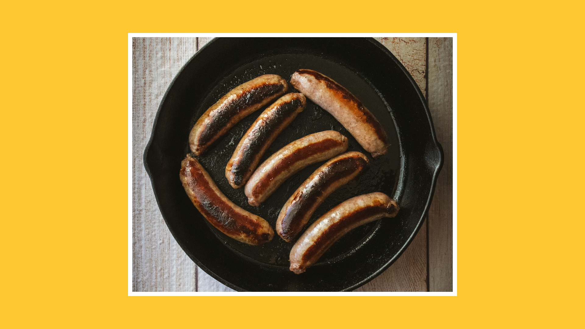 “Pan of browned sausages cooking in a skillet on a wooden surface