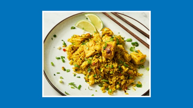“Plate of chicken fried rice with spring onions, herbs and a wedge of lime.”