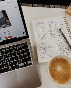 A topdown view of a laptop, notepad and coffee