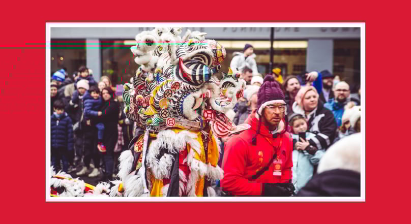 Chinese New Year lion dance performer in a detailed costume moving through a crowded city street.