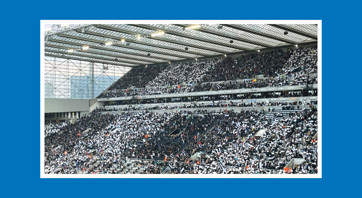 Crowd inside St James’ Park stadium waving black-and-white flags during a match.