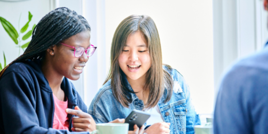 Two students sat with coffee cups looking at phone