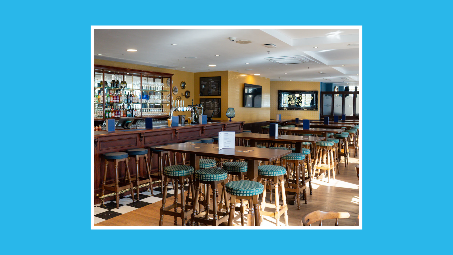 Empty pub interior of the Golden Flake with wooden tables, high stools, a bar lined with taps, and daylight streaming through windows