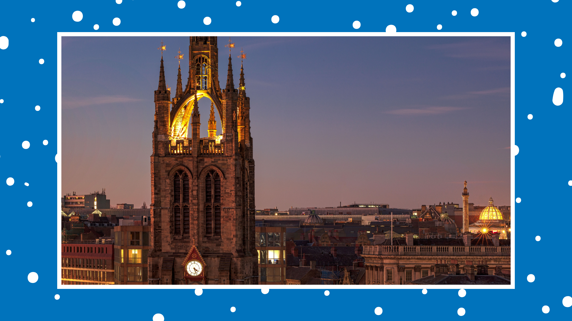 Illuminated cathedral tower at dusk overlooking a city skyline, with historic buildings and rooftops in the foreground