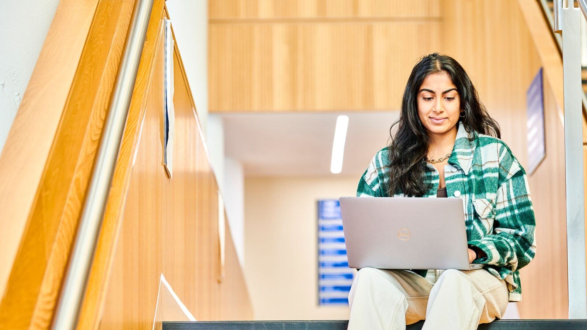 A student sat on top of stairs, working on a laptop