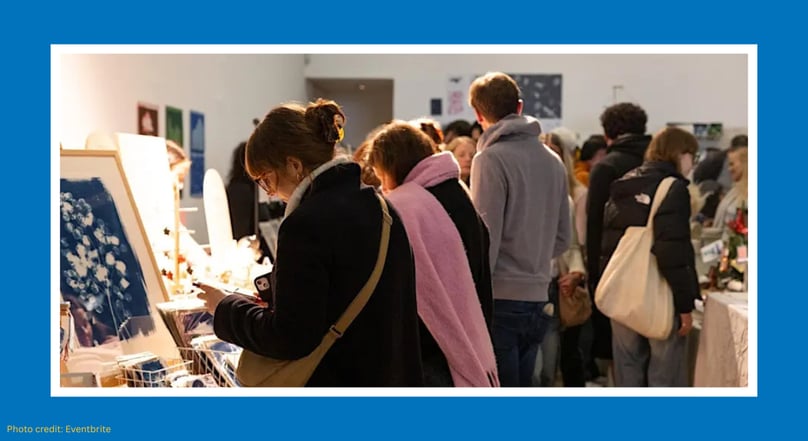 People browsing art and handmade items at an indoor makers market.