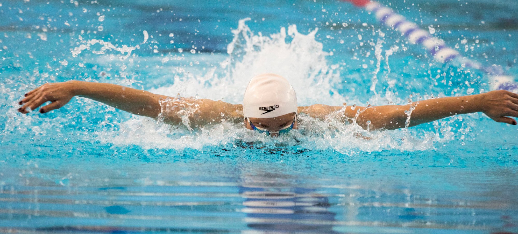 A swimmer, mid-stroke doing the butterfly with a white swimming cap